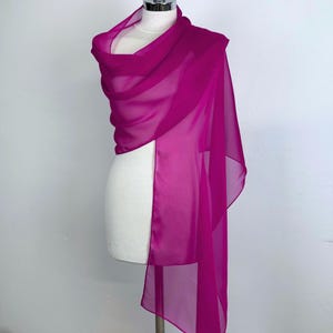 Puede incluir: Un chal de gasa rosa fucsia drapeado sobre un maniqu&iacute; blanco. El chal est&aacute; hecho de una tela ligera y fluida.