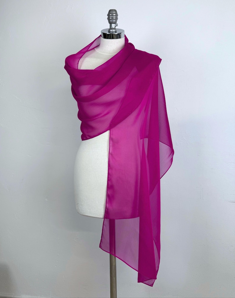 Puede incluir: Un chal de gasa rosa fucsia drapeado sobre un maniqu&iacute; blanco. El chal est&aacute; hecho de una tela ligera y fluida.