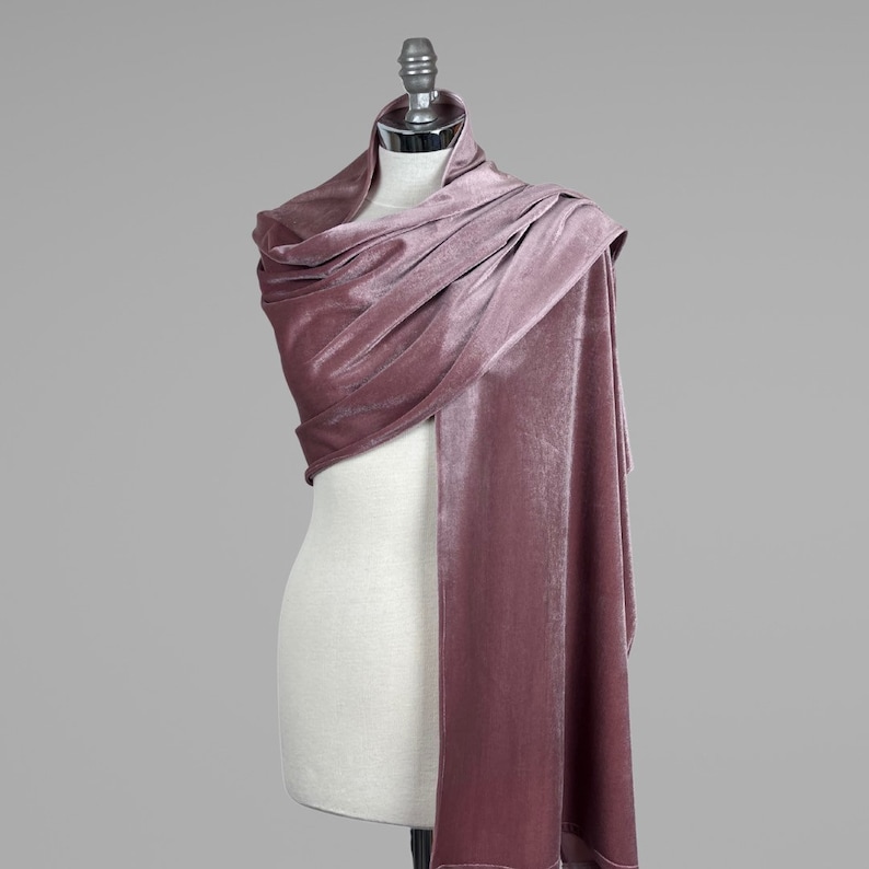 May include: A dusty rose velvet shawl draped over a mannequin. The shawl is soft and luxurious, perfect for adding a touch of elegance to any outfit.