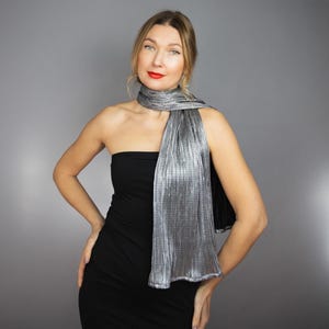 Może przedstawiać: Kobieta w czarnej sukni bez ramiączek i srebrnym, plisowanym szaliku. Szalik jest zawiązany wokół szyi i opada na klatkę piersiową.