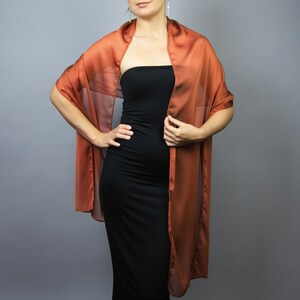 May include: A sheer, russet-coloured shawl draped over a black dress. The shawl has a flowing, rectangular shape, with the fabric cascading down the front. The overall look is elegant and suitable for formal occasions.