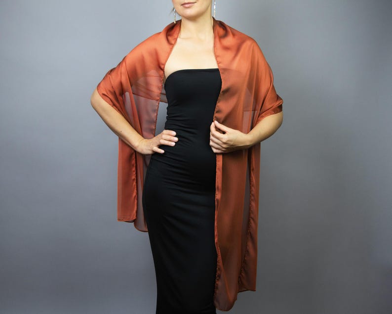 May include: A sheer, russet-coloured shawl draped over a black dress. The shawl has a flowing, rectangular shape, with the fabric cascading down the front. The overall look is elegant and suitable for formal occasions.