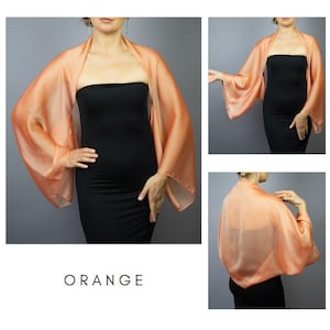 Pu&ograve; includere: Uno scialle di seta arancione con maniche ampie. Lo scialle &egrave; drappeggiato su un vestito nero. La parola "ORANGE" &egrave; stampata in bianco in basso nell'immagine. Lo scialle &egrave; un tessuto leggero e fluido.