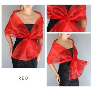 May include: A red sheer shawl with a bow tied in the front. The shawl is made of a lightweight fabric and is perfect for adding a touch of elegance to any outfit.