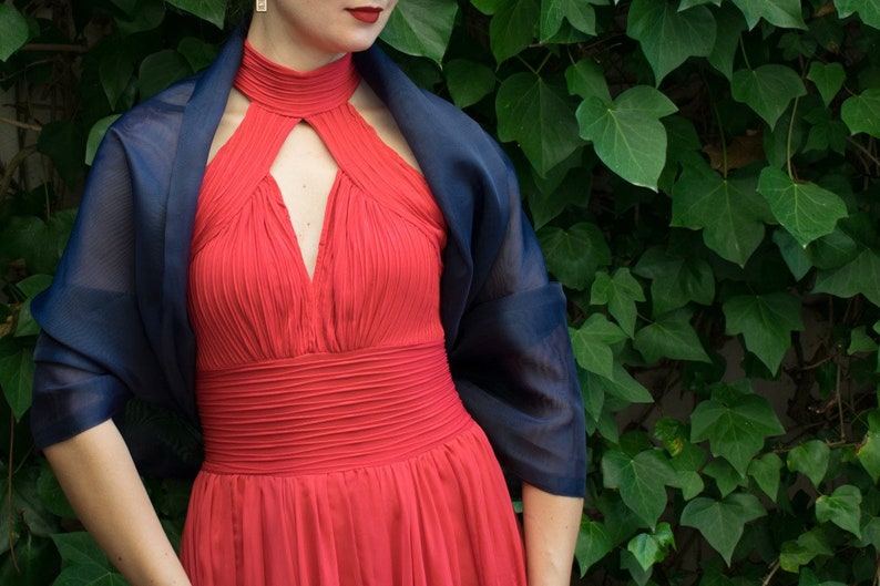 May include: A woman wearing a red halter dress with a navy blue shawl draped over her shoulders.