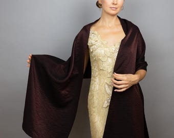 Pode incluir: Uma mulher vestindo um vestido de renda dourado com um xale de cetim bordô drapeado sobre os ombros.