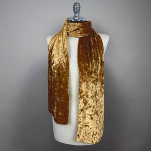 Puede incluir: Una bufanda de terciopelo dorado arrugado. La bufanda se muestra en un maniquí blanco.