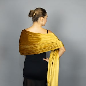 Peut inclure: Châle en velours jaune moutarde drapé sur une robe noire. Le châle est enroulé autour des épaules et des bras, avec une extrémité pendante. Le tissu a un aspect doux et luxueux, et la couleur est riche et vibrante.