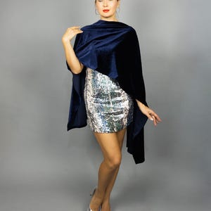 May include: A navy blue velvet cape draped over a silver sequined mini dress. The cape has a soft, flowing texture. Silver pointed-toe heels complete the look, creating an elegant ensemble.