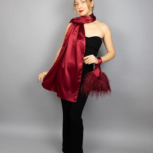 May include: A woman wearing a strapless black top and black pants with a long, burgundy satin scarf draped around her neck. She is holding a small, burgundy feather clutch.
