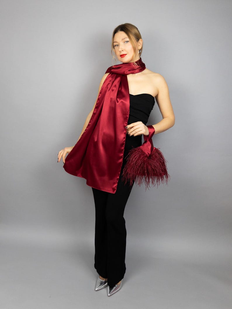May include: A woman wearing a strapless black top and black pants with a long, burgundy satin scarf draped around her neck. She is holding a small, burgundy feather clutch.