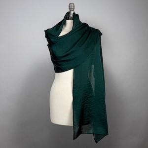 May include: A dark green silk scarf draped over a white mannequin. The scarf is soft and flowing, and it would be perfect for adding a touch of elegance to any outfit.