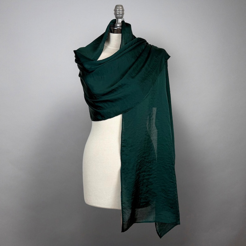 May include: A dark green silk scarf draped over a white mannequin. The scarf is soft and flowing, and it would be perfect for adding a touch of elegance to any outfit.