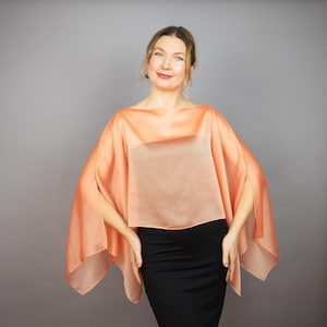Puede incluir: Una blusa transparente de color melocotón con un escote amplio y fluido y mangas largas. La blusa está hecha de una tela ligera y tiene un corte holgado.