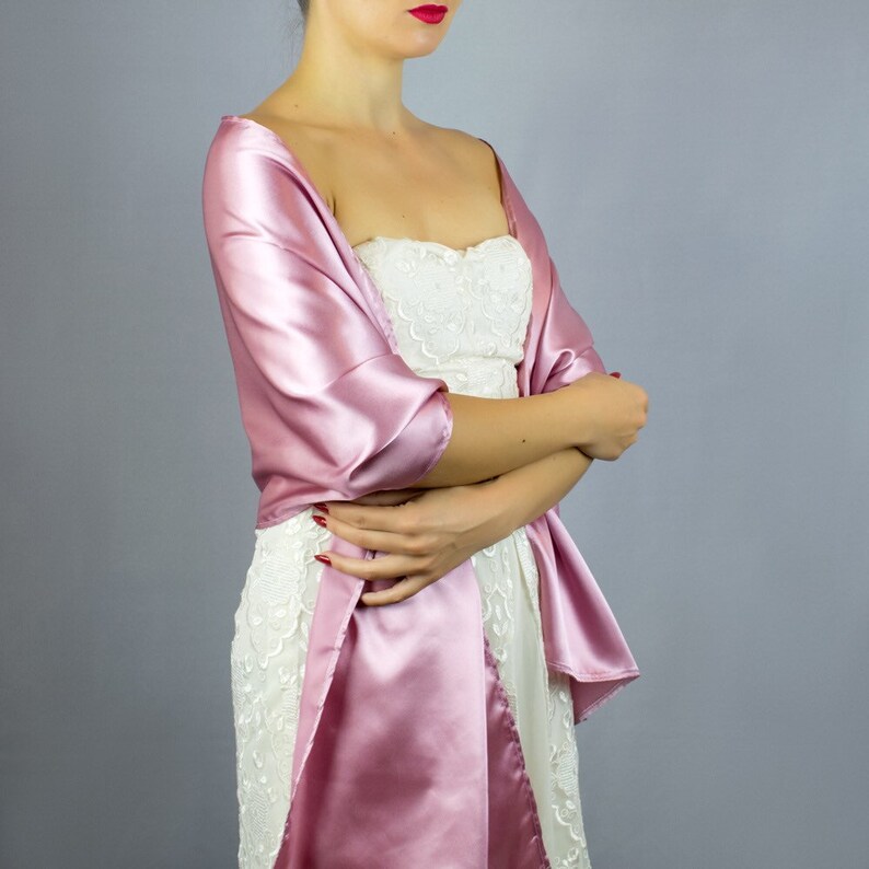 May include: A pink satin shawl draped over a white lace dress. The shawl is tied at the neck and falls down the front of the dress.