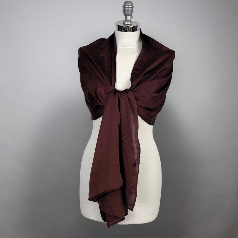 May include: A burgundy satin shawl draped over a white mannequin. The shawl is tied in a knot at the front and the ends are left to hang down.