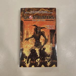 May include: A paperback book titled "Ghostbusters: The Return" by Sholly Fisch. The cover features a menacing creature and Ghostbusters figures against a fiery backdrop. Text at the top reads "Never Before Published 20th Anniversary Ghostbusters Event!"