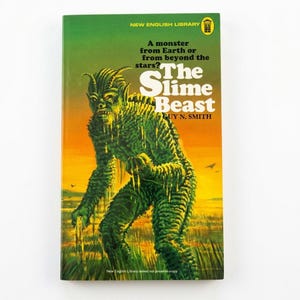 Peut inclure: Un livre de poche intitulé The Slime Beast de Guy N. Smith, illustré d'un monstre vert texturé debout dans un champ sous un ciel au coucher du soleil jaune et orange. La couverture porte le texte A monster from Earth or from beyond the stars?
