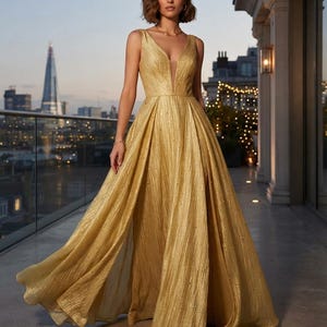 May include: A floor-length sleeveless gold gown featuring a deep V-neckline with a sheer mesh insert, a fitted bodice with vertical pleats, and a voluminous, pleated skirt with a subtle shimmering texture and scattered light-reflecting embellishments.