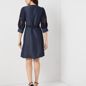 May include: A navy blue dress with a V-neck and a matching belt. The sleeves are three-quarter length with openwork detailing. The dress is knee-length and is paired with black high-heeled shoes.