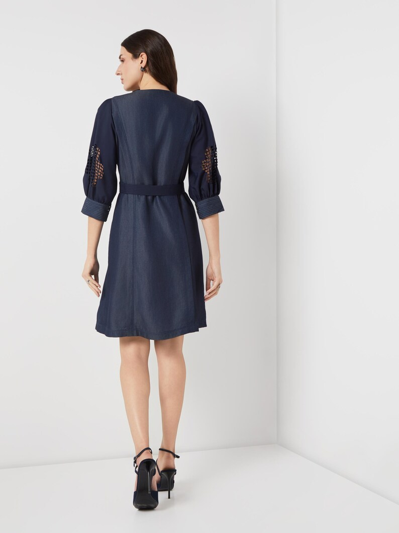 May include: A navy blue dress with a V-neck and a matching belt. The sleeves are three-quarter length with openwork detailing. The dress is knee-length and is paired with black high-heeled shoes.