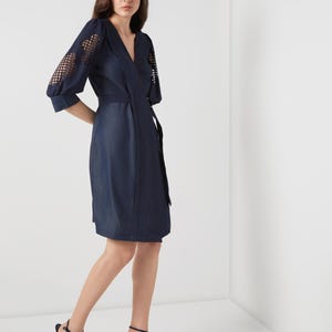 May include: A navy blue wrap dress with a V-neckline and a matching belt. The sleeves feature a unique openwork design. The model is wearing navy blue high-heeled sandals.