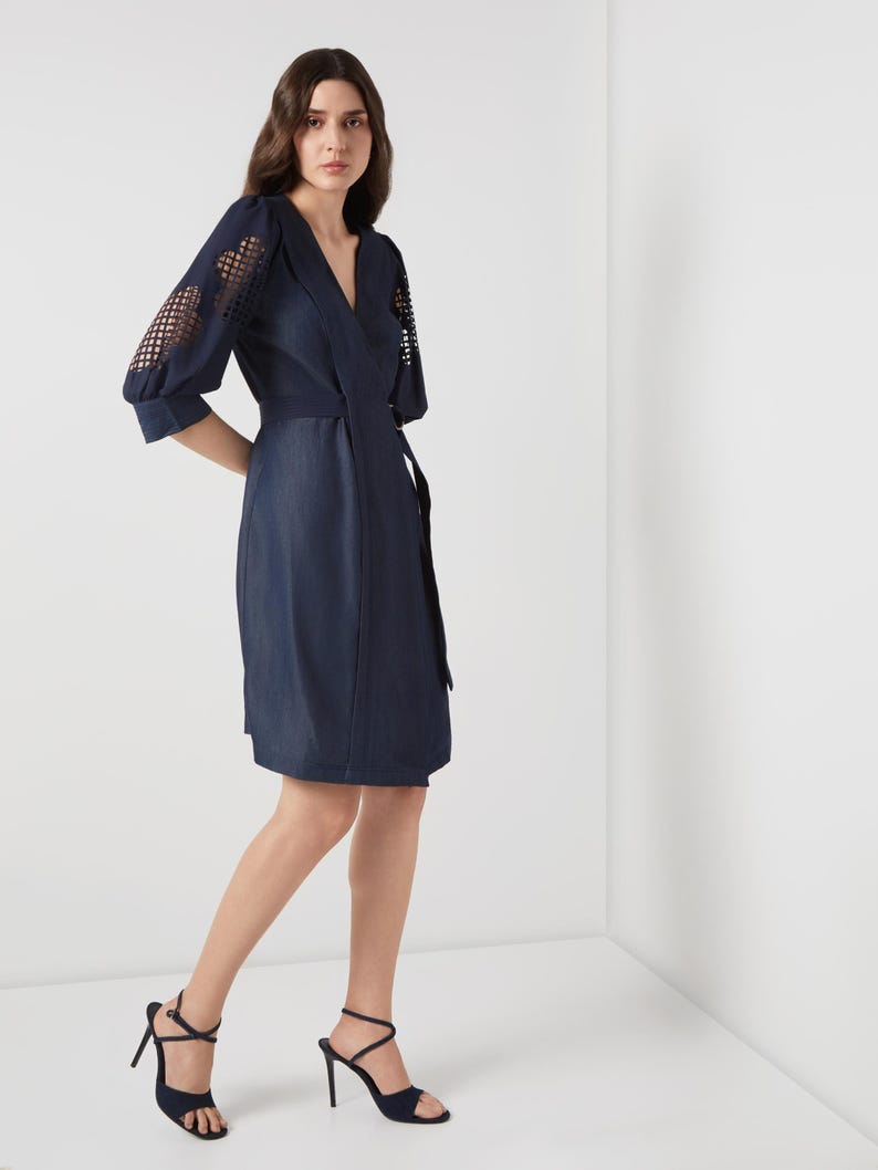 May include: A navy blue wrap dress with a V-neckline and a matching belt. The sleeves feature a unique openwork design. The model is wearing navy blue high-heeled sandals.