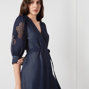 May include: A dark blue wrap dress with a V-neckline and a matching belt. The sleeves feature a unique cut-out design. The dress is made of a denim-like fabric and has a flowing skirt. The overall style is elegant and modern.
