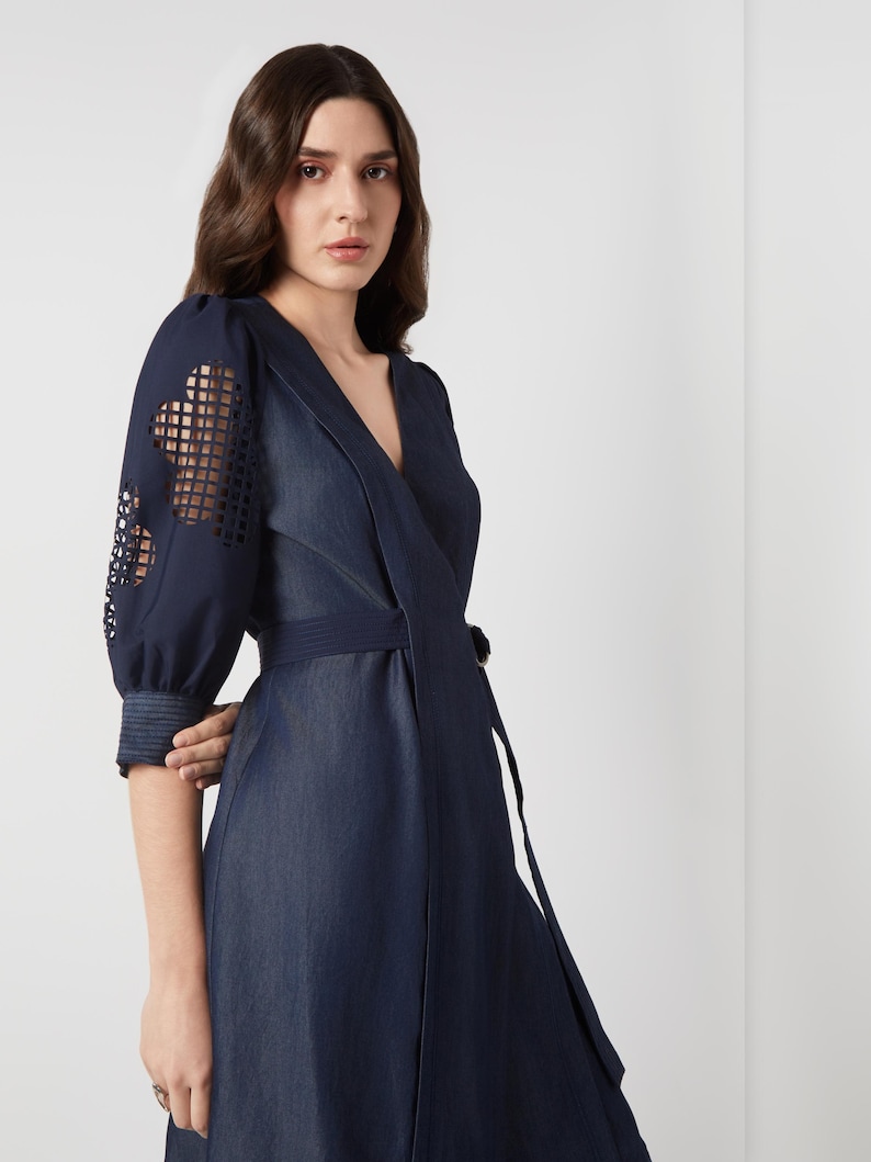 May include: A dark blue wrap dress with a V-neckline and a matching belt. The sleeves feature a unique cut-out design. The dress is made of a denim-like fabric and has a flowing skirt. The overall style is elegant and modern.