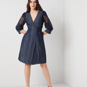 May include: A dark blue wrap dress with a V-neckline and a belt. The dress features sheer, open-weave sleeves and a knee-length skirt. The model is wearing black high-heeled sandals.