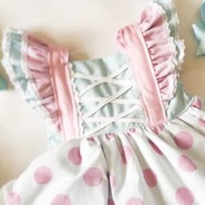 May include: A light blue and pink polka dot dress with white lace trim and pink ruffles on the straps. The dress has a white criss-cross back.