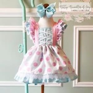 May include: A blue and pink polka dot dress with a white lace trim and pink ruffle sleeves. The dress has a criss-cross bodice and is styled with a blue bow.