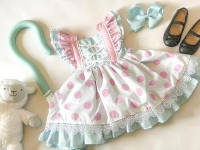 May include: A blue and pink polka dot dress with white lace trim and pink ruffles. The dress has a white criss-cross bodice and comes with a matching blue bow and a shepherd's crook.