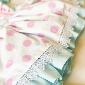 May include: Close-up of a white and pink polka dot fabric with a light blue ruffle and white lace trim.