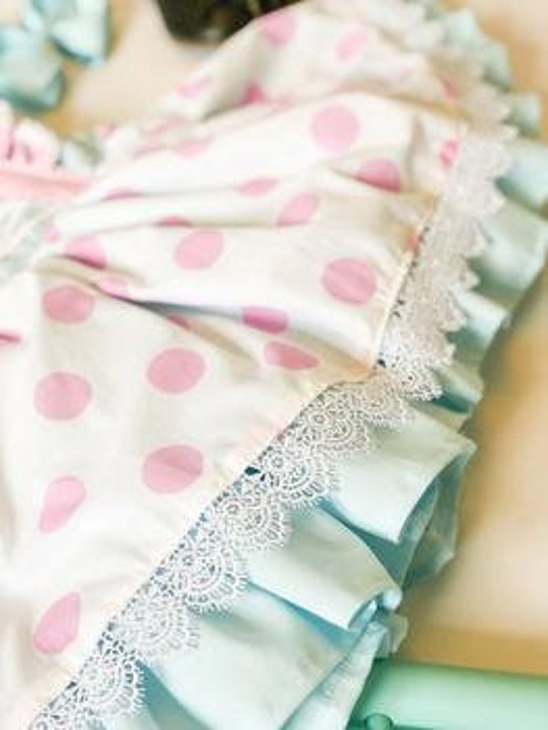 May include: Close-up of a white and pink polka dot fabric with a light blue ruffle and white lace trim.