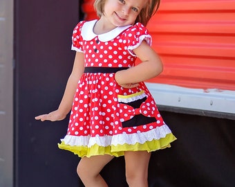 May include: A young girl wearing a red and white polka dot dress with black accents and a yellow ruffle trim. She is wearing black shoes and has red bows in her hair.