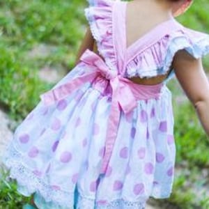 May include: A white and pink polka dot dress with a pink bow on the back. The dress has a ruffled neckline and a lace trim.
