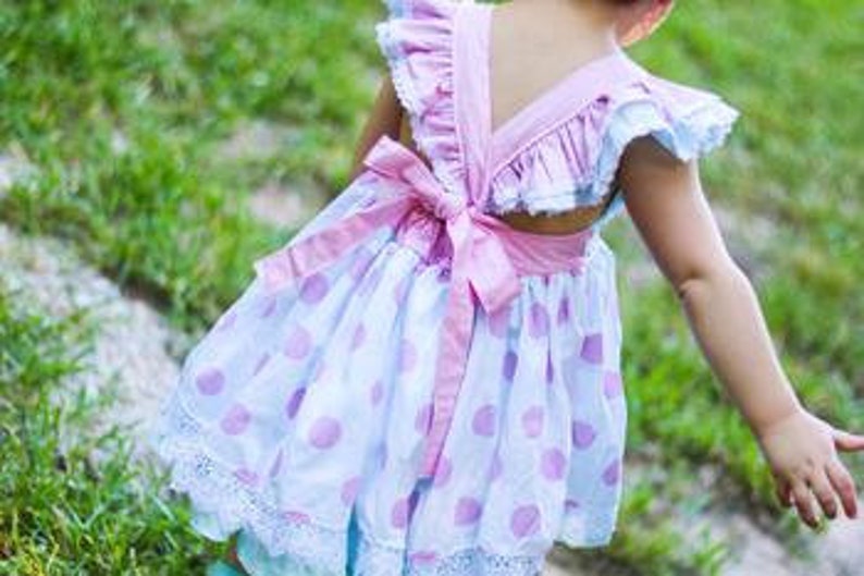 May include: A white and pink polka dot dress with a pink bow on the back. The dress has a ruffled neckline and a lace trim.