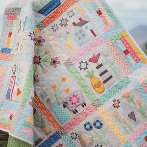 May include: A colorful patchwork quilt with various embroidered designs. The quilt features squares with images of a house, flowers, a sheep, and other decorative elements. The color palette includes pastel shades of pink, blue, green, and yellow.