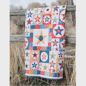 Könnte beinhalten: Ein farbenfroher Quilt mit Sternenmuster, der rote, weiße, blaue und gelbe Sterne auf einem Patchwork-Design zeigt. Der Quilt ist über einem Holzzaun drapiert und zeigt seine komplizierten Details und leuchtenden Farben. Der Quilt misst ca. 152 cm x 178 cm.