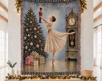 Könnte beinhalten: Eine gewebte Wandteppich-Decke mit einer Ballerina in einem Spitzenkleid, die einen Nussknacker hält, sowie einem geschmückten Weihnachtsbaum, verpackten Geschenken und einer Standuhr. Der Text The Nutcracker steht oben in einer Schreibschrift.
