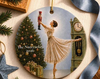 Könnte beinhalten: Ein runder Keramikschmuck mit einer Ballerina in einem cremefarbenen Spitzenkleid, die eine Nussknacker-Figur hält. Ein geschmückter Weihnachtsbaum mit Geschenken und eine Standuhr sind abgebildet. Der Text lautet The Nutcracker 2026.