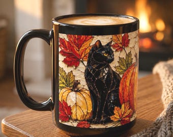 May include: A black ceramic mug featuring a stained glass style illustration of a black cat sitting between two pumpkins surrounded by vibrant red, orange, and yellow autumn leaves. The mug is filled with a light brown beverage with foam on top.