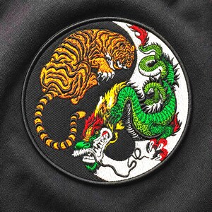 Pode incluir: Patch bordado circular com um design yin-yang apresentando um tigre e um dragão. O tigre é laranja e preto, o dragão é verde, vermelho e amarelo. O patch tem uma borda preta.