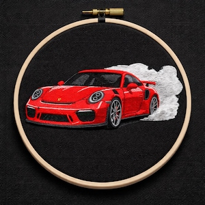 May include: Embroidered red sports car with white smoke detail, set in a wooden embroidery hoop against a black background. The car features detailed stitching, showcasing its design. A unique piece of automotive art.