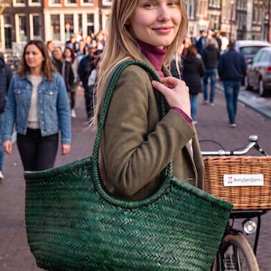 Op de afbeelding: Een grote, donkergroene geweven tas met een gestructureerde gevlochten textuur en twee geïntegreerde ronde handvatten. De tas heeft een breed ontwerp met een open bovenkant en een consistent, ingewikkeld visgraatpatroon over de gehele buitenkant.