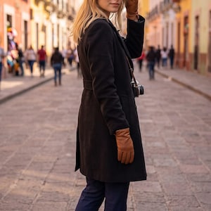 Intrecciato woven leather gloves in cognac brown on a woman's hand, paired with a black coat on a sunlit city street.