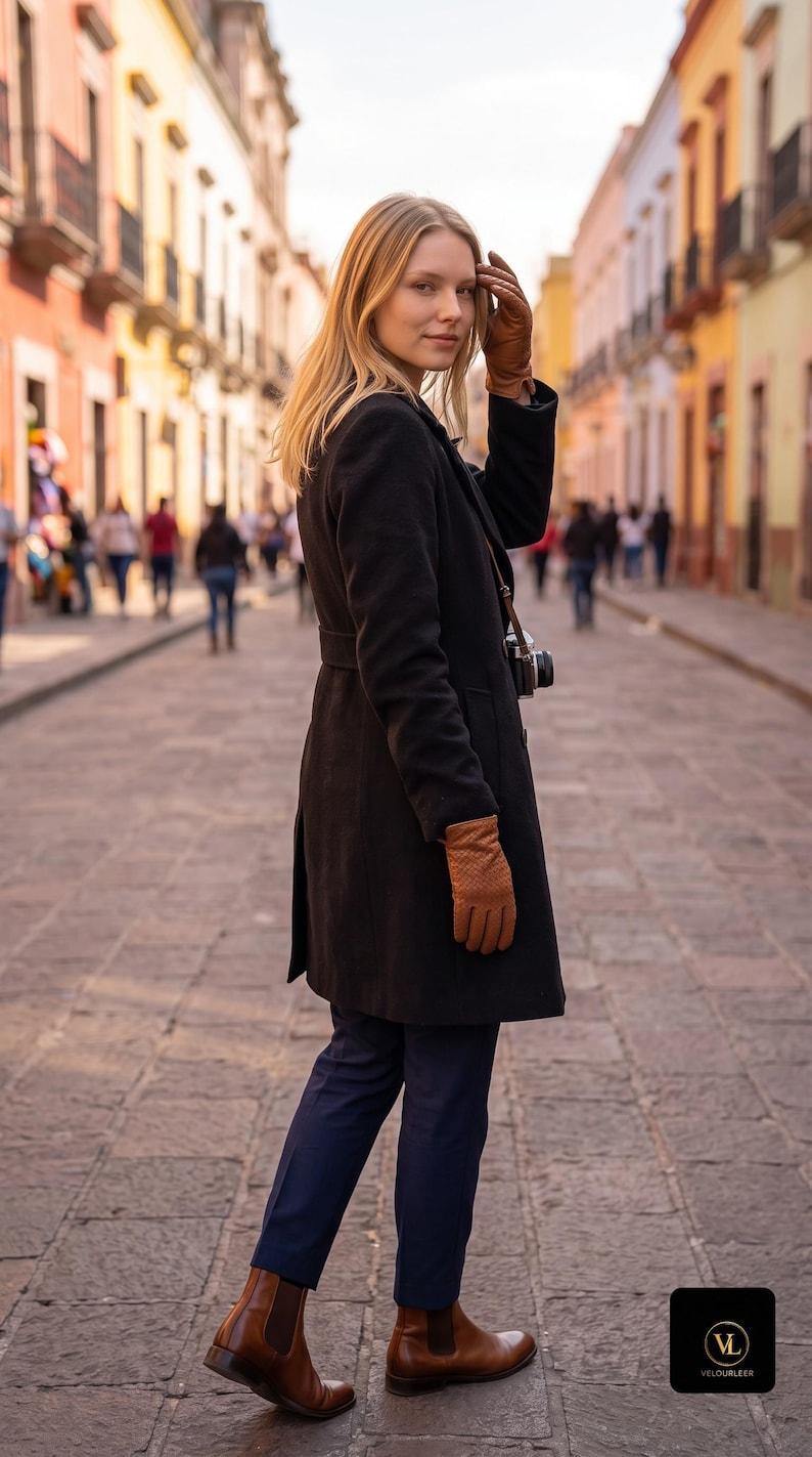 Intrecciato woven leather gloves in cognac brown on a woman's hand, paired with a black coat on a sunlit city street.