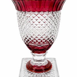 Puede incluir: Un florero de vidrio transparente y rojo rubí con un borde acampanado, un patrón de corte de diamante en el cuerpo y una base cuadrada. El borde superior y la sección inferior del pedestal son de color rojo intenso, mientras que el cuerpo es de vidrio tallado.