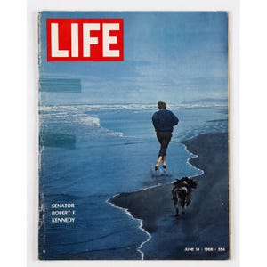 Pode incluir: Uma capa de revista LIFE vintage datada de 14 de junho de 1968, apresentando uma fotografia em tons de azul de uma pessoa correndo ao longo de uma praia de areia escura com um cão. O logótipo vermelho LIFE está no topo, com o texto SENATOR ROBERT F. KENNEDY.